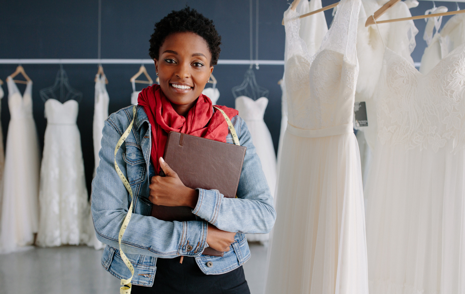 woman inside bridal store surrounded by bridal dresses while holding a notebook